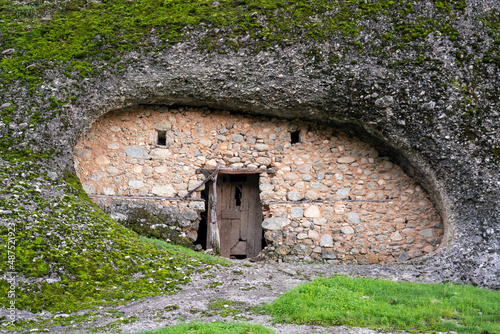 Tableau sur toile An old dwelling under a hill overgrown with grass and vegetation in the middle, an old door and two small windows
