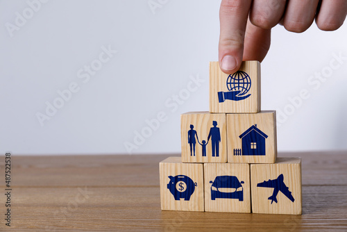 Man building pyramid of cubes with different icons on wooden table against light background, closeup. Insurance concept