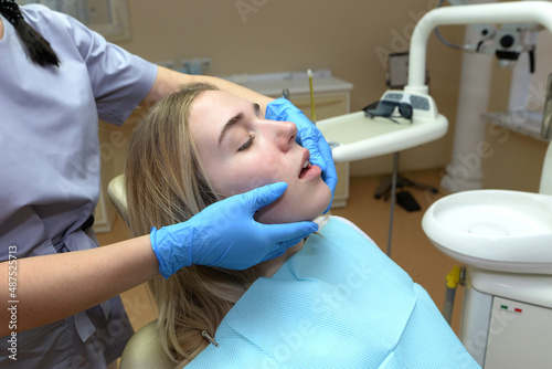 European young woman sits in a medical chair while a dentist examines her teeth in a dental clinic.