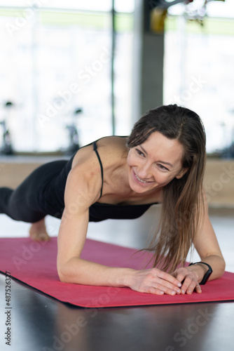 middle-aged woman is standing in plank position on yoga mat in the studio