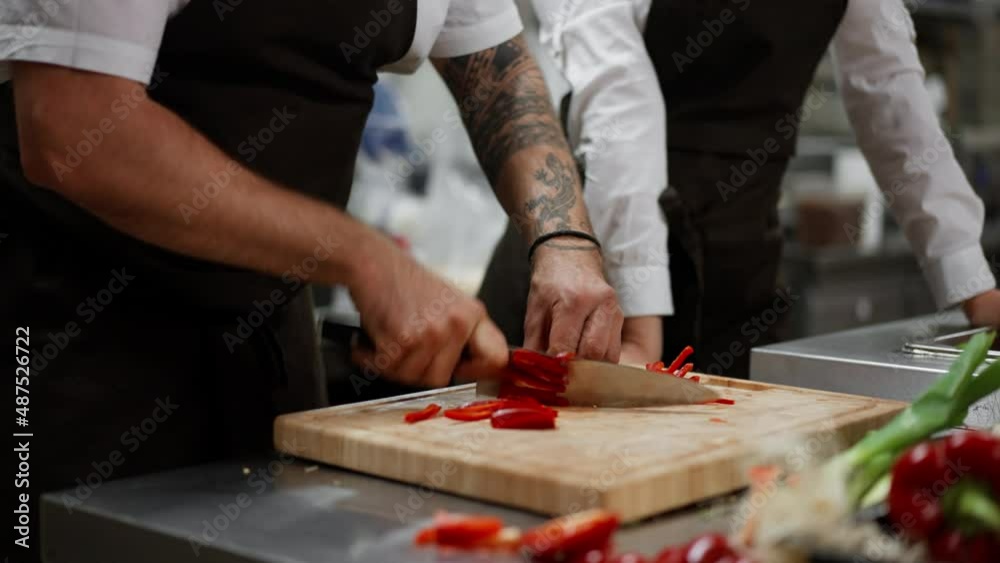 Close-up of unrecognizable chef cutting vegetables indoors in commercial kitchen.