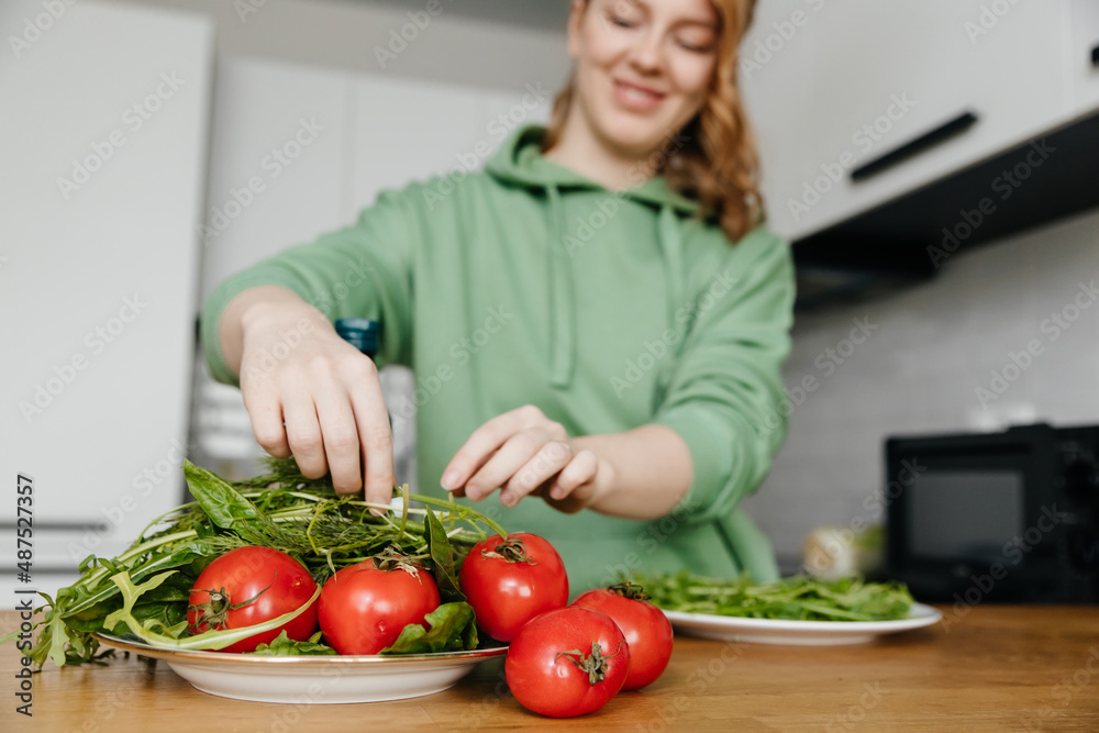 Woman preparing fresh vegetable salad in the kitchen with modern interior. Focus in the foreground.