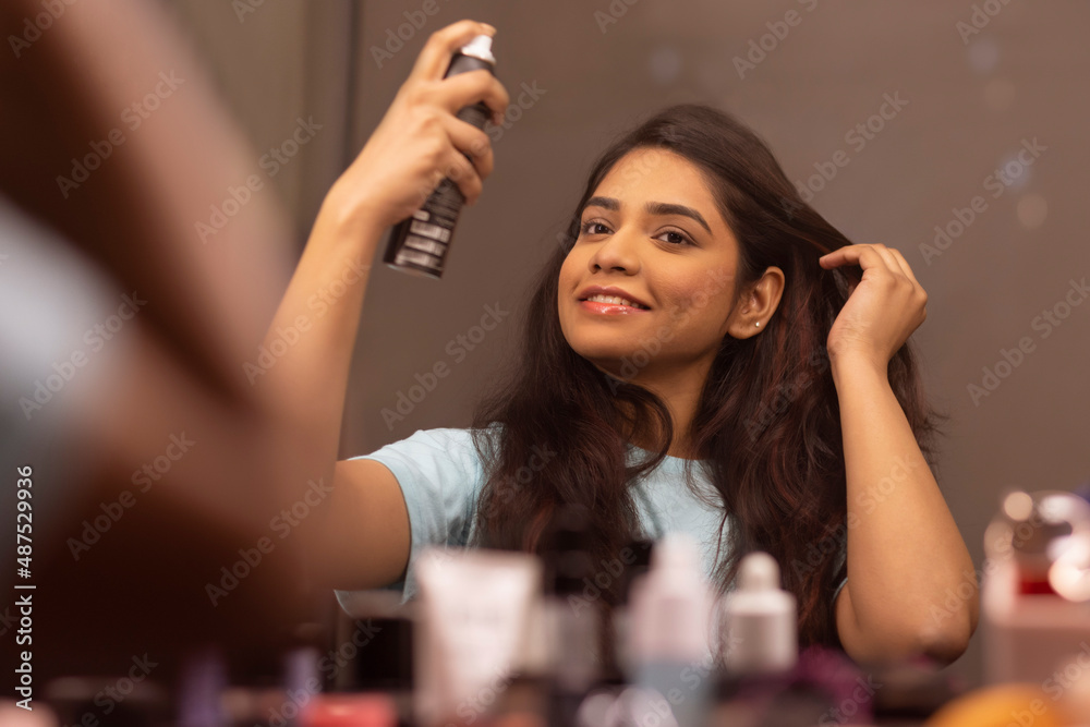 Young woman applying face toner while doing make up in front of mirror