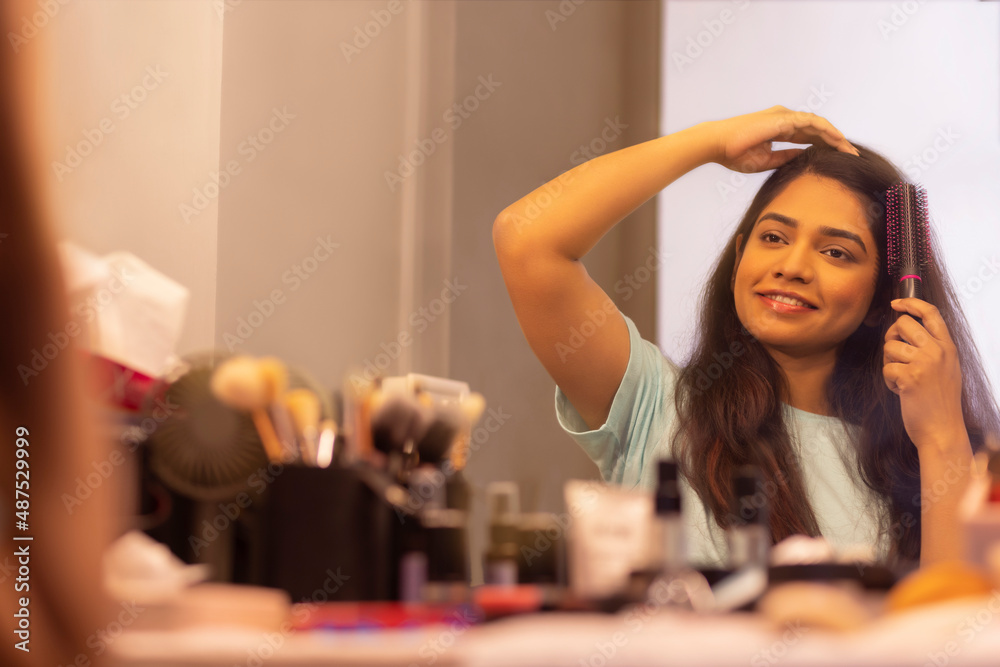 Young woman combing her hair in front of mirror
