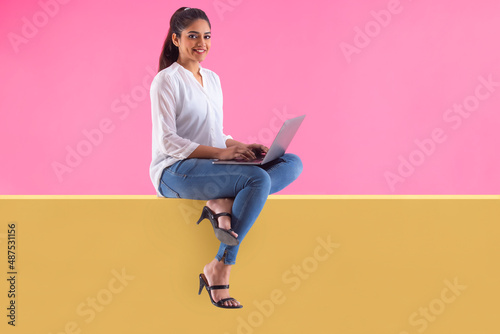 Bild auf Leinwand Woman with laptop on lap sitting on wall and looking at camera with smile