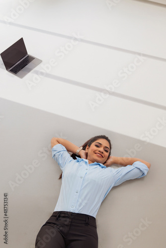 Young business woman in formal outfit lying on floor with hands behind neck