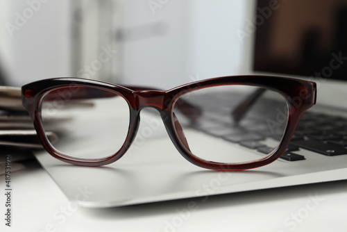 Modern laptop and glasses on white table, closeup