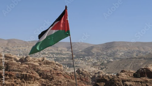 Petra Jordan FEBRUARY, 2, 2018: Jordan flag waving in the air on a sunny and windy day in Petra landscape. Monastery in the ancient city of Petra. Mountains against the clear blue sky.  photo