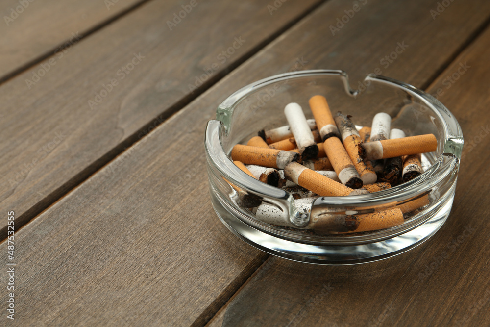 Glass ashtray with cigarette stubs on wooden table. Space for text Glass ashtray with cigarette stubs on wooden table. Space for text