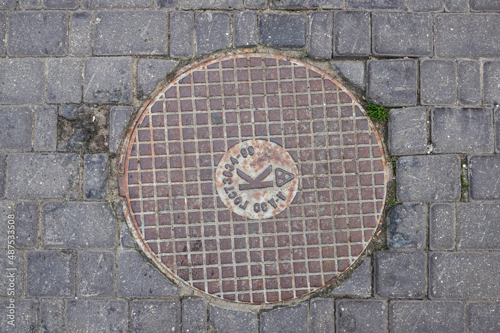 Old metal manhole cover sewer cap on the city street Translation: Abbreviation for State Standard, Sewerage.