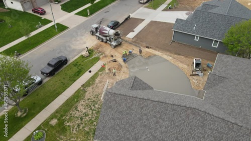 Overhead view of concrete crew working together to finish driveway of new home construction project. Concrete mixer truck adding more wet cement.