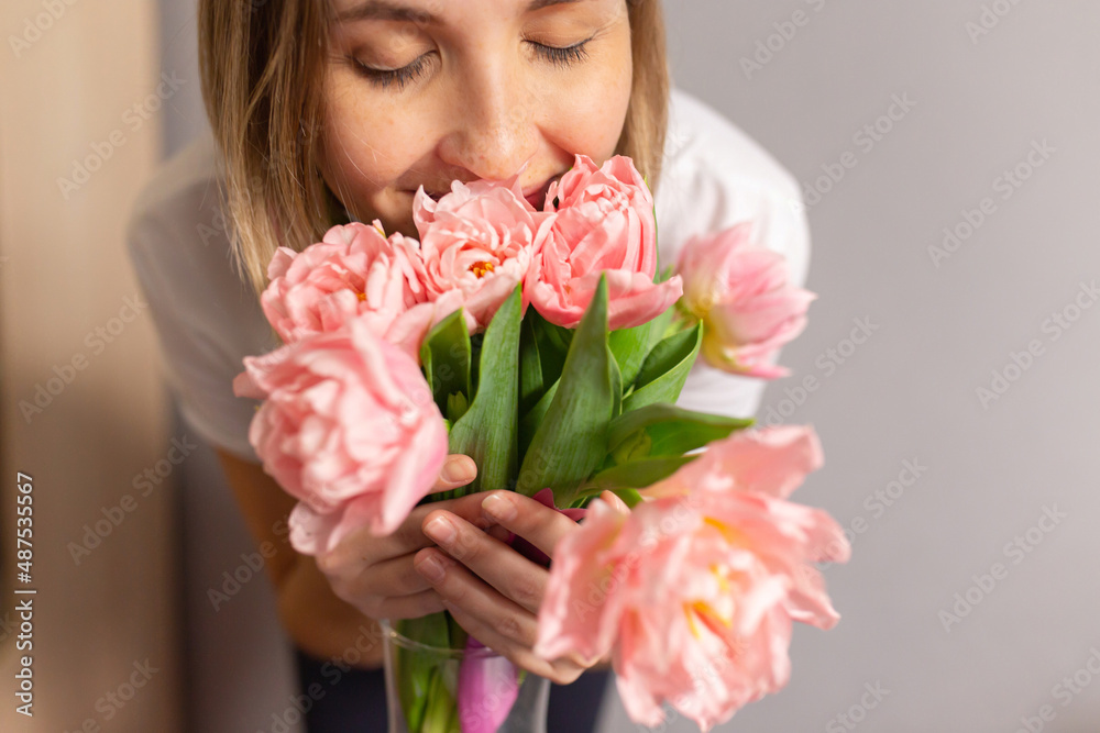 Girl sniffing pink tulips in a glass vase. March 8, Valentine's day, birthday wife, date, flowers for a woman. Close-up