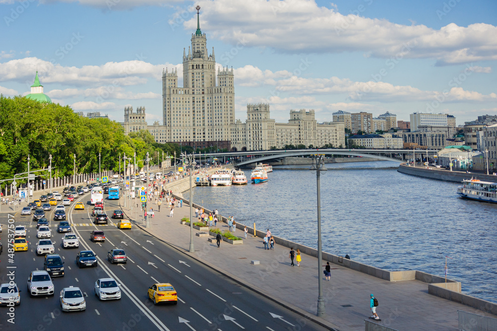 Moscow, Russia - June 16, 2019: Traffic of cars on Moskvoretskaya embankment from height of floating bridge in Zaryadye park. In background is Stalinist skyscraper on Kotelnicheskaya Embankment.