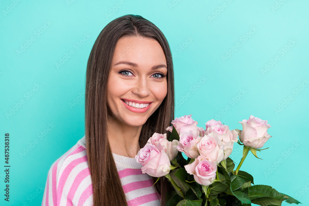 Portrait of attractive cheerful sweet cute girl smelling fresh pink roses isolated over bright teal turquoise color background Portrait of attractive cheerful sweet cute girl smelling fresh pink roses isolated over bright teal turquoise color background