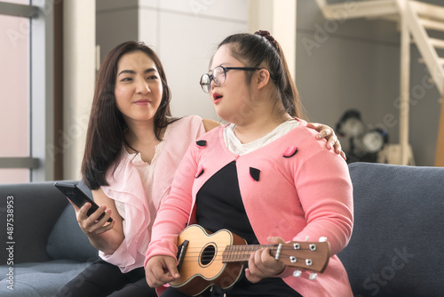 girl with autism is watching smartphone for playing ukulele and singing with his mother. Autistic young students are learning with teachers happily. Training for intelligence restoration for autism.