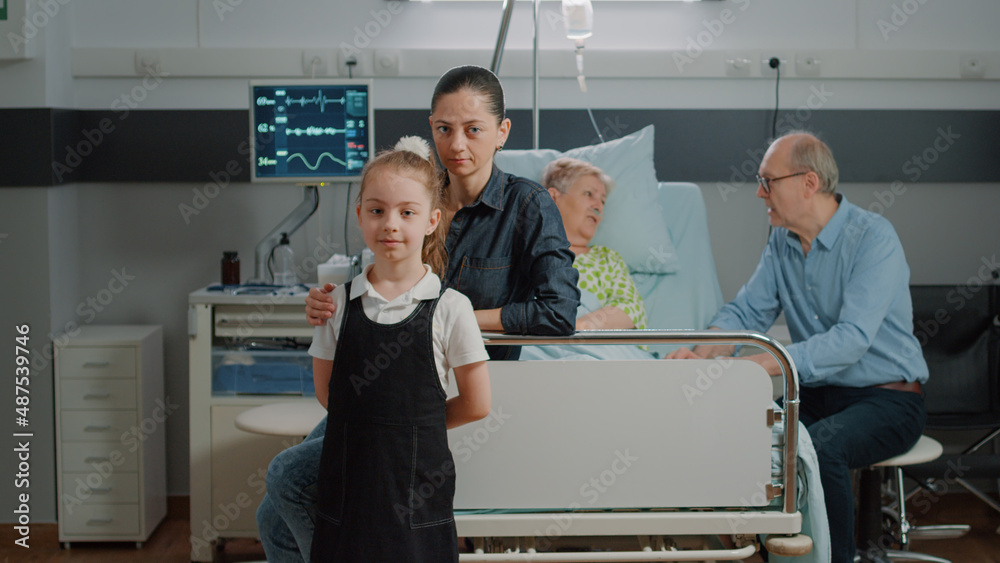 Obraz premium Portrait of child and mother visiting old patient in hospital ward bed. Woman and kid sitting in intensive care room at family visit, giving support to pensioner with sickness at clinic.