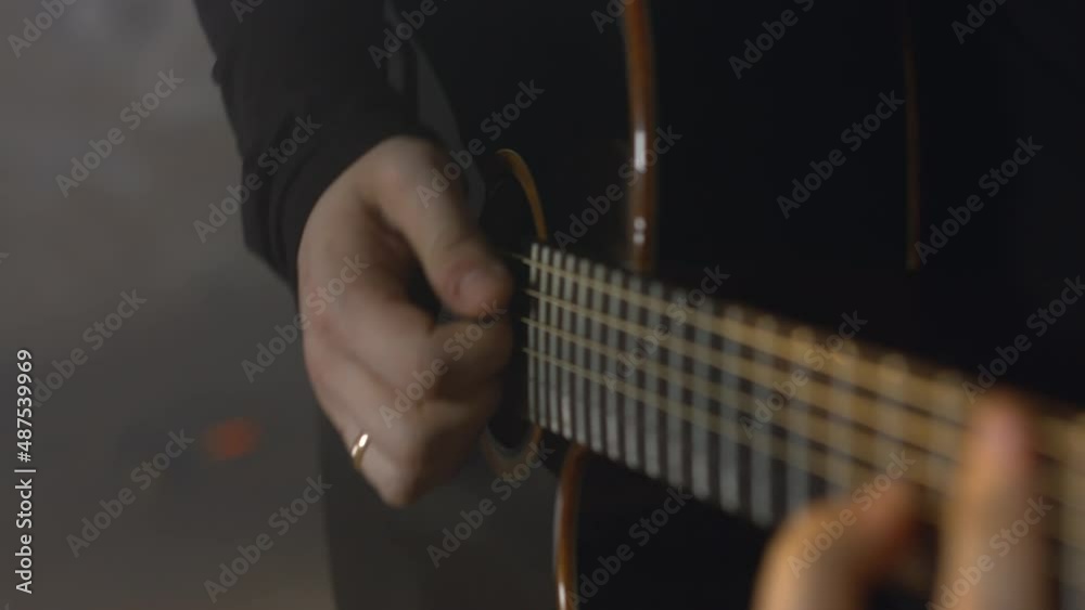 A European man in a black sweatshirt plays the acoustic guitar. Caucasian guy pinches a chord on the strings A European man in a black sweatshirt plays the acoustic guitar. Caucasian guy pinches a chord on the strings