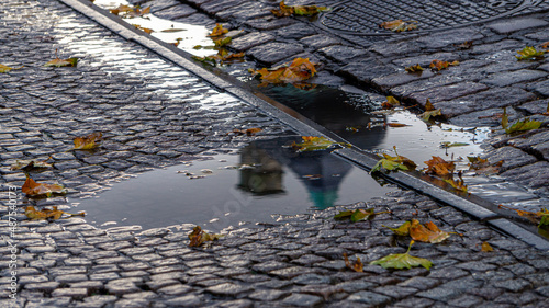 Puddle of water with a wet cobblestone floor, with the reflection of a building and full of autumn leaves.