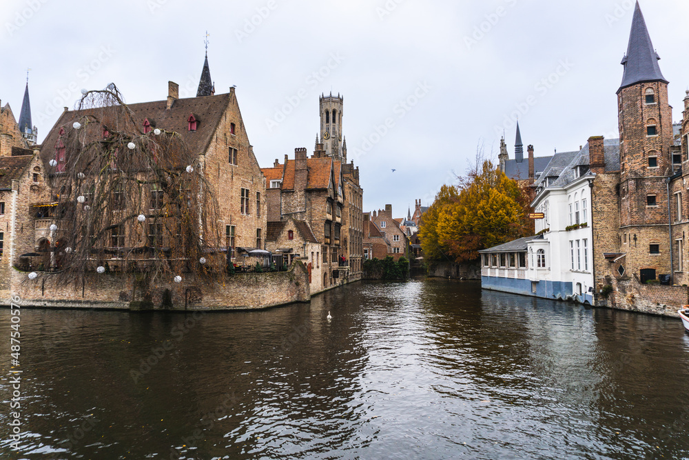 Panorama of Bruges, where there is a water channel, at the bottom of the image the church tower and typical Belgian houses. Cloudy day with autumn colors.