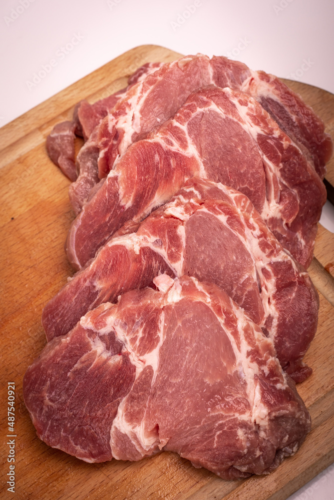 Pork meat cut into chops, slices, on a wooden chopping board, on a white. Raw pork neck steaks, cutlets, close up. Pork meat cut into chops, slices, on a wooden chopping board, on a white. Raw pork neck steaks, cutlets, close up.