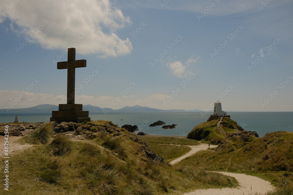cross on the top of the hill with lighthouse in the background during summer on Anglesey island