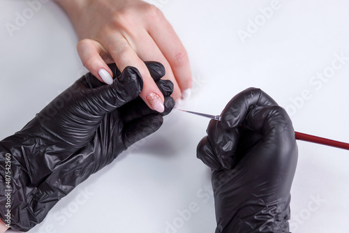 Partial view of manicurist in latex black gloves applying nail polish while making manicure to client on blurred foreground. Fine brush manicure nail polish  modeling gel.