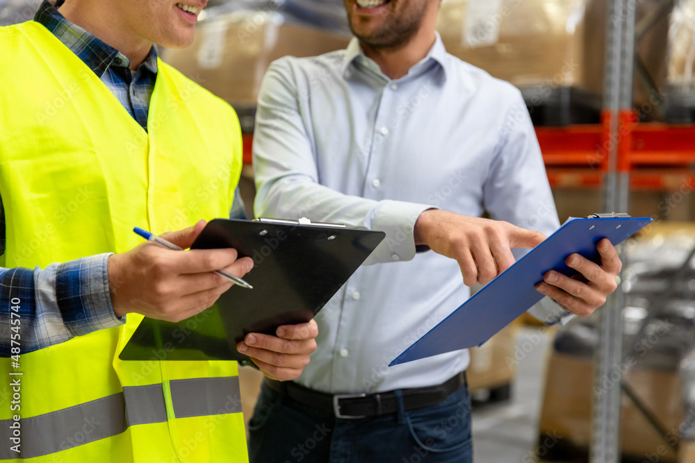 wholesale, logistic business and people concept - close up of manual worker and businessman with clipboards at warehouse wholesale, logistic business and people concept - close up of manual worker and businessman with clipboards at warehouse
