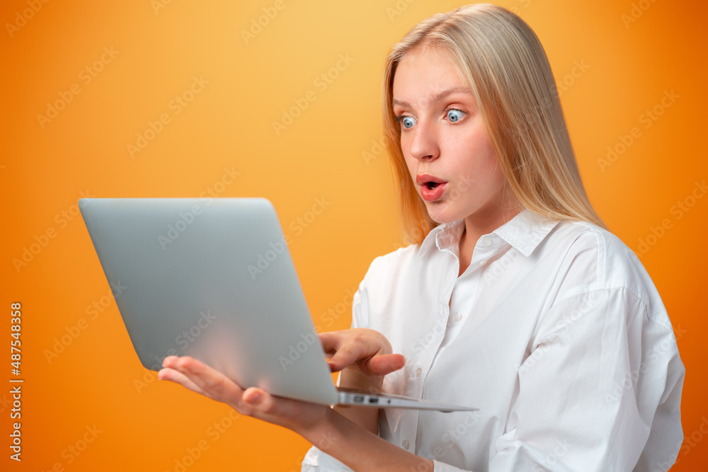 Portrait of a cheerful young teen girl holding laptop computer against orange background