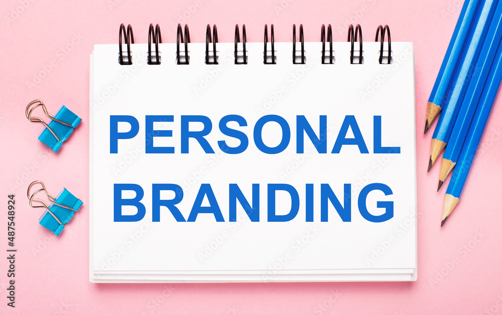 On a light pink background, light blue pencils, paper clips and a white notebook with the text PERSONAL BRANDING On a light pink background, light blue pencils, paper clips and a white notebook with the text PERSONAL BRANDING
