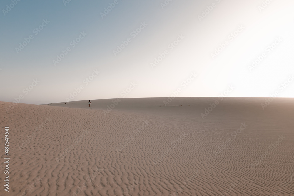 Naklejka premium Chica caminando por la arena de las dunas en Fuerteventura durante el atardecer