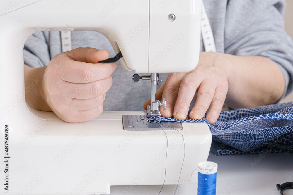 Seamstress makes a seam on an electric sewing machine. Close-up of hands. Tailor workflow details.