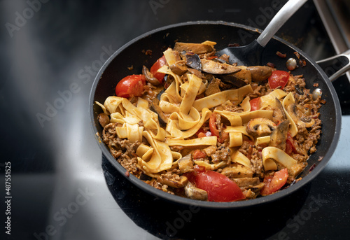 Pasta pan from tagliatelle and sauce Bolognese style with minced meat, tomatoes and vegetables on the black stove, copy space, selected focus