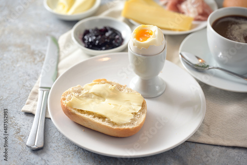 Bread roll with butter, cooked egg, jam and coffee on a breakfast table, selected focus