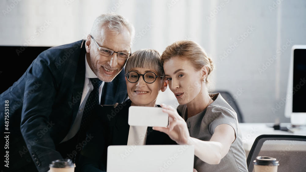 Smiling business people taking selfie on smartphone in office Smiling business people taking selfie on smartphone in office