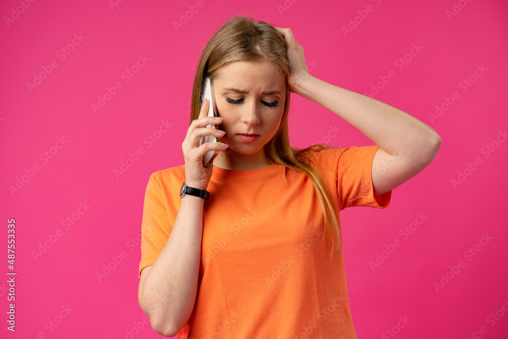 Upset young woman talking on the phone disappointed over pink background Upset young woman talking on the phone disappointed over pink background