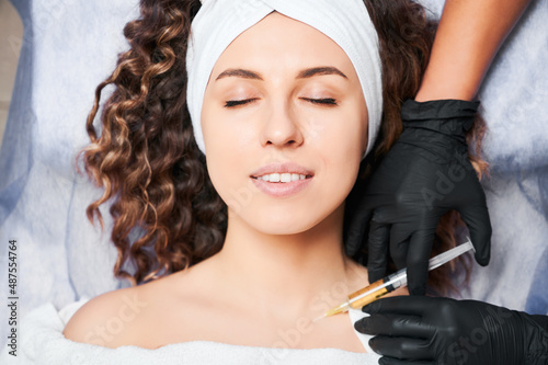Cosmetologist's hands starting procedure of biorevitalization of decollete area for young curly woman. Anti aging skin rejuvenation procedure. Injections of beauty.