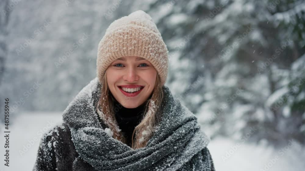 Happy young woman in winter under falling snow in nature looking at camera Happy young woman in winter under falling snow in nature looking at camera