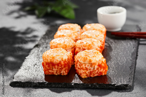 Baked Maki sushi on dark slate. Hot california maki with tobiko. Sushi roll with masago caviar, cheese topped baked oven. Style concept japanese menu with black background, leaves and hard shadow.