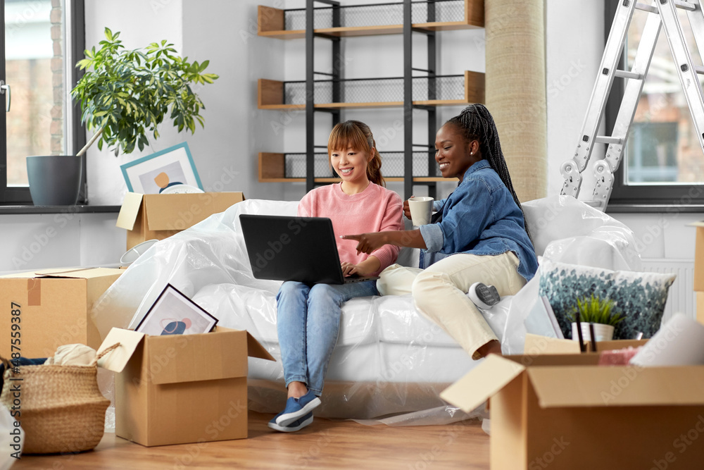 moving, people and real estate concept - happy smiling women with laptop computer and boxes at new home moving, people and real estate concept - happy smiling women with laptop computer and boxes at new home