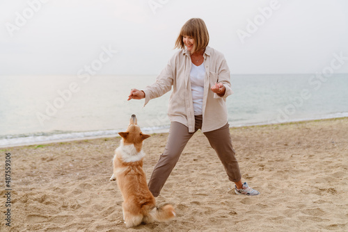 Senior woman laughing and playing with her dog while resting on beach