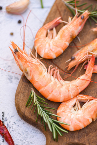boiled shrimp prawns cooked in the seafood restaurant, fresh shrimps wooden cutting board plate with ice herbs and spices lemon chili rosemary on table background