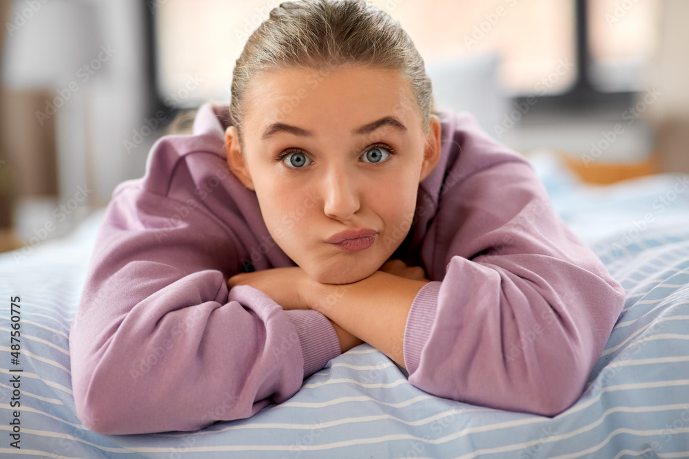 emotion, expression and people concept - girl lying on bed at home and making face emotion, expression and people concept - girl lying on bed at home and making face