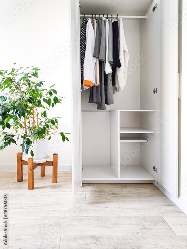 Wardrobe with basic clothes in room scandi interior. Neutral colors: white, black, beige. 