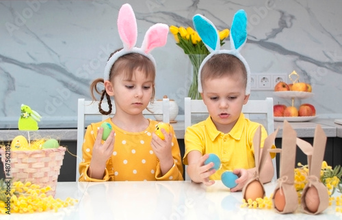 happy Easter! funny kids with bunny ears are getting ready for the holiday. A child, a boy and a girl, wear bunny ears and play with colorful eggs