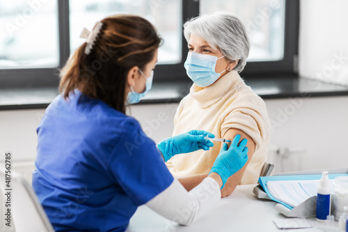 medicine, health and vaccination concept - doctor or nurse with syringe making vaccine or drug injection to senior woman in mask at hospital © Syda Productions