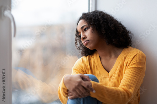 Photography Depressed young African American woman sitting near window, looking outside on s