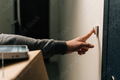 Fotografija Close-up hands of unrecognizable delivery man ringing doorbell of customer apartment holding cardboard box, contactless payment POS wireless terminal for card paying