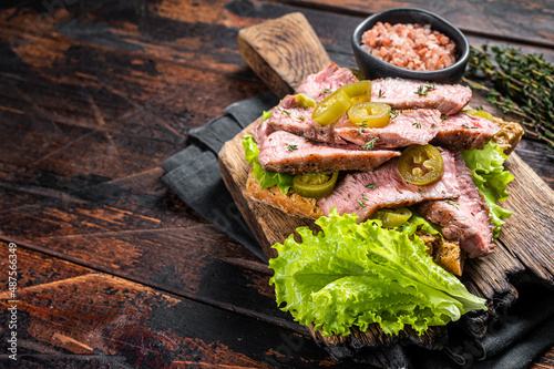Beef Steak sandwich with sliced griiled beef, salad and vegetables on bread. Wooden background. Top view. Copy space