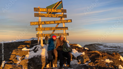 Foto A happy hiker sits on top of Mount Kilimanjaro with his black guide