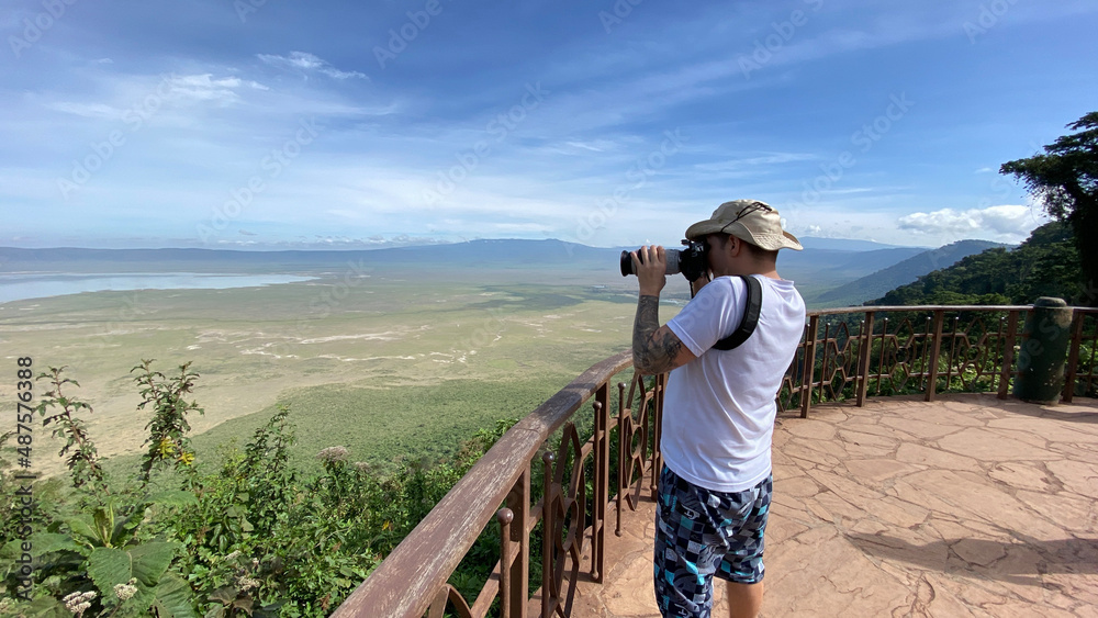 A white guy in a panama hat with a big camera stands on the observation deck of the Ngorongoro National Park.